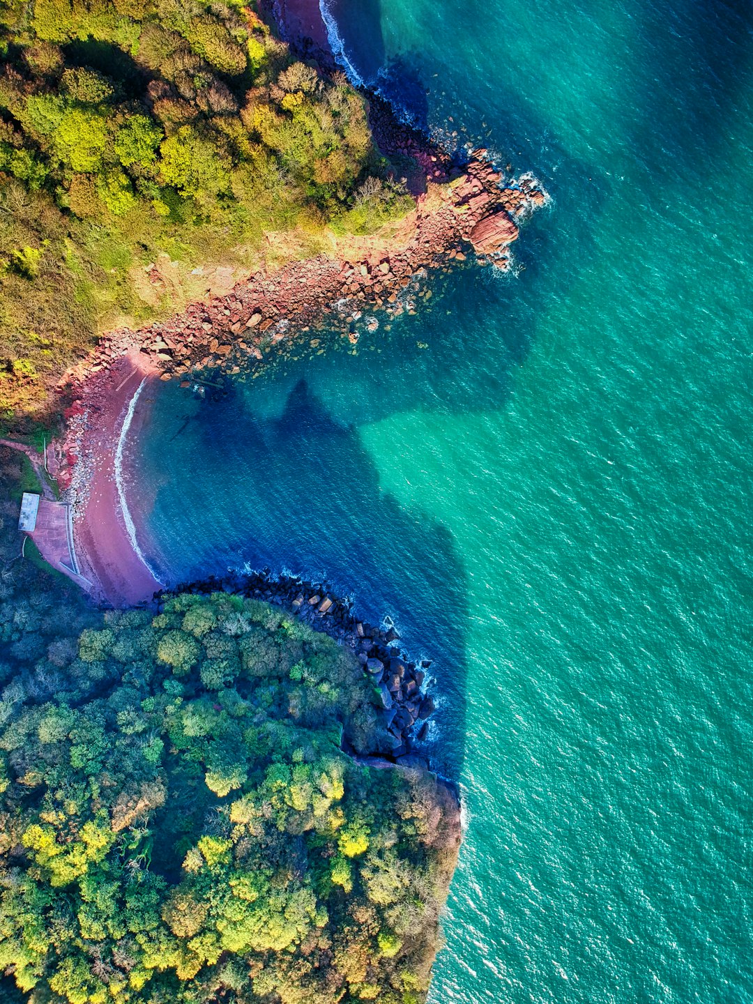 Turquoise ocean meets secluded beach with rocky cliffs.