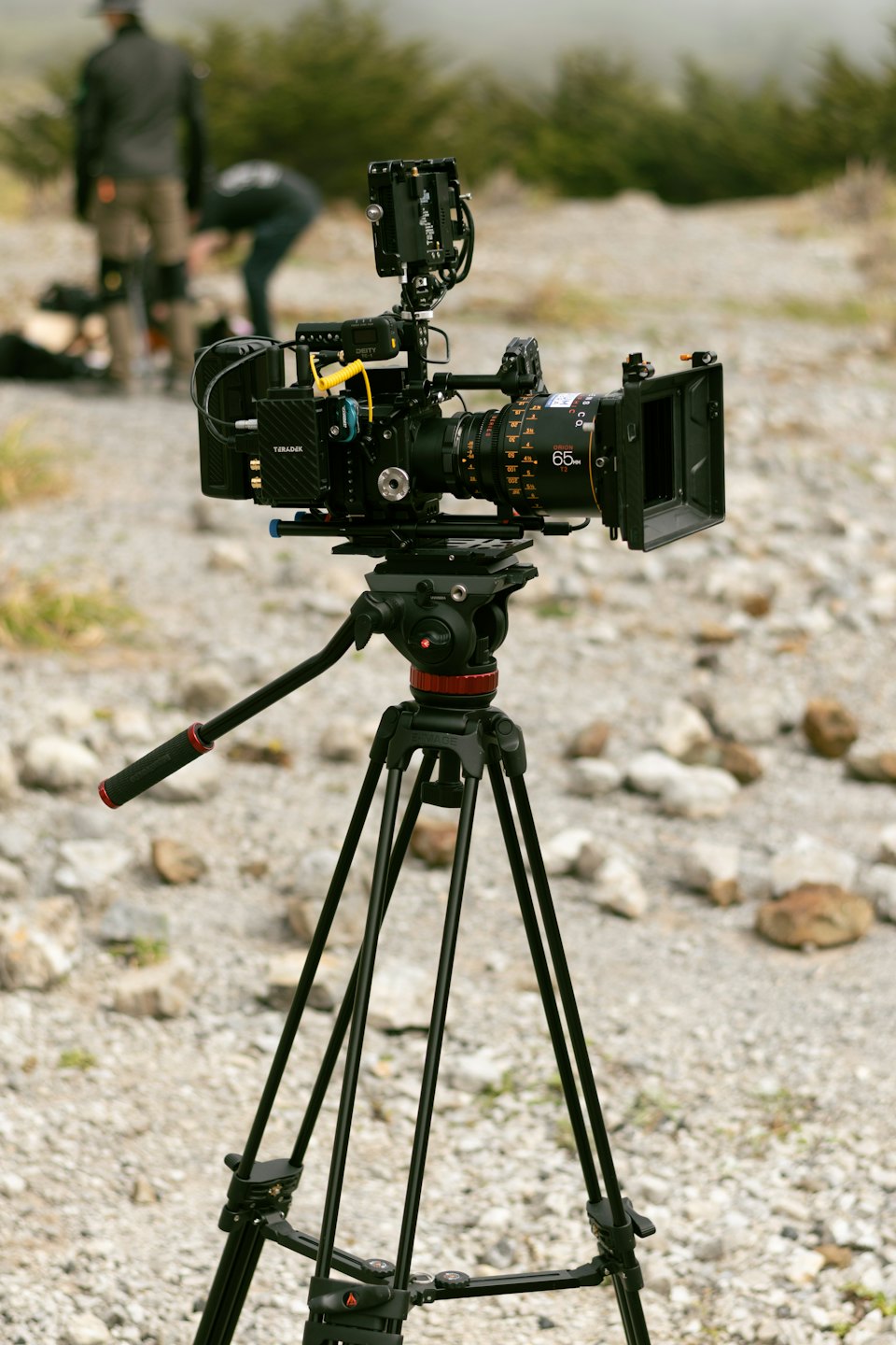 Professional video camera on a tripod in rocky terrain.