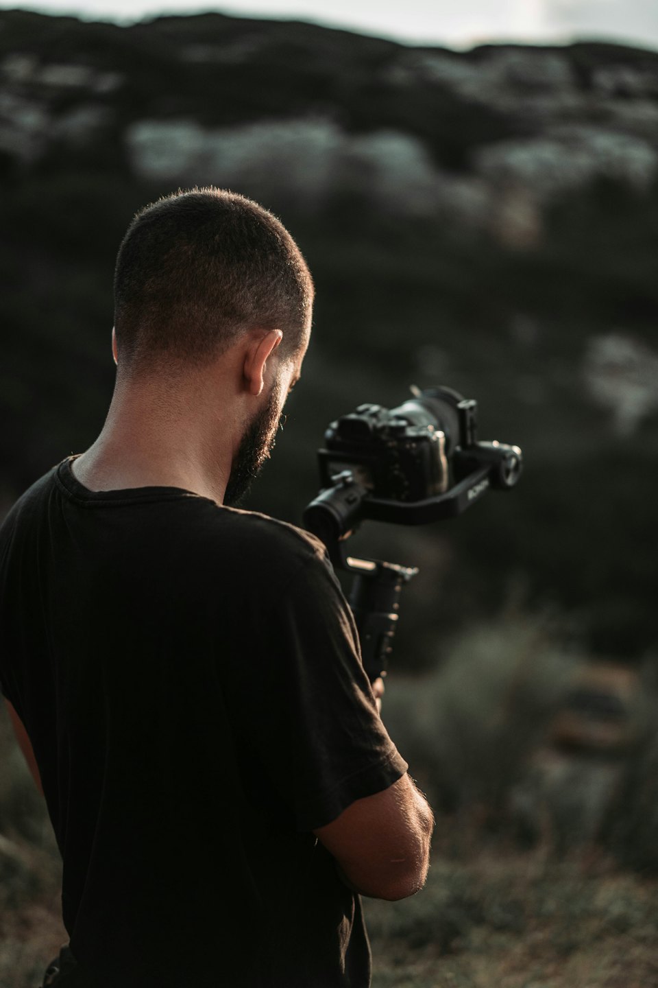 Filmmaker uses a professional gimbal camera outdoors near hills.